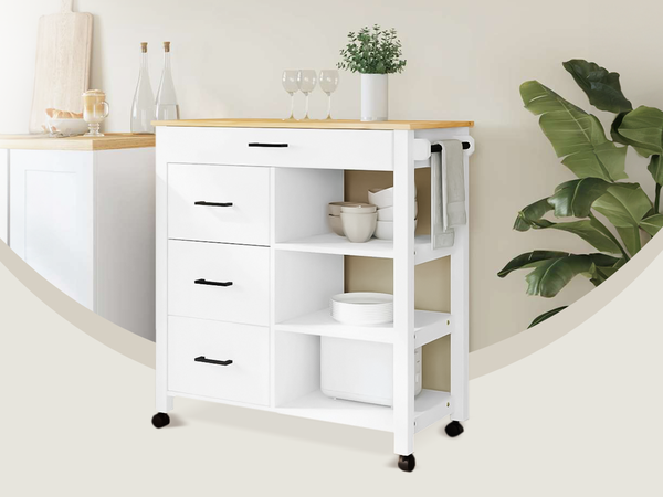 White storage trolley with shelves, drawers and a wooden top placed in a styled kitchen corner next to a large green plant. Click to see the products in the collection.