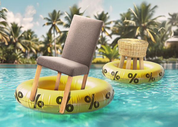 A gray dining chair and a small round wicker stool each balancing on yellow inflatable rings patterned with black percent signs, in a pool with tropical palm trees in the background.