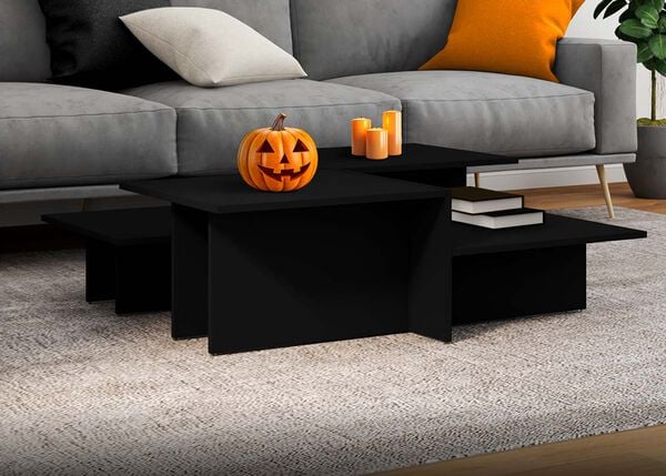 Black nested coffee tables with a carved pumpkin and orange candles, next to a grey sofa with pillows in a styled living room. 