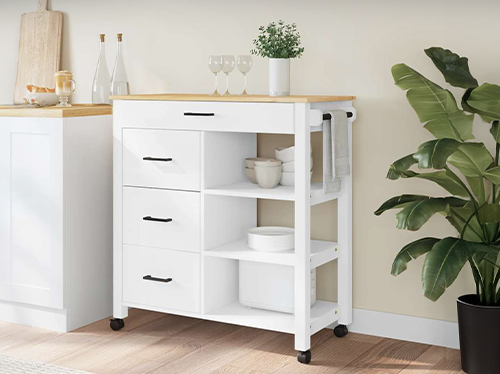 White storage trolley with shelves, drawers and a wooden top placed in a styled kitchen corner next to a large green plant. Click to see the products in the collection.