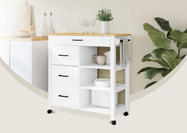 White storage trolley with shelves, drawers and a wooden top placed in a styled kitchen corner next to a large green plant.