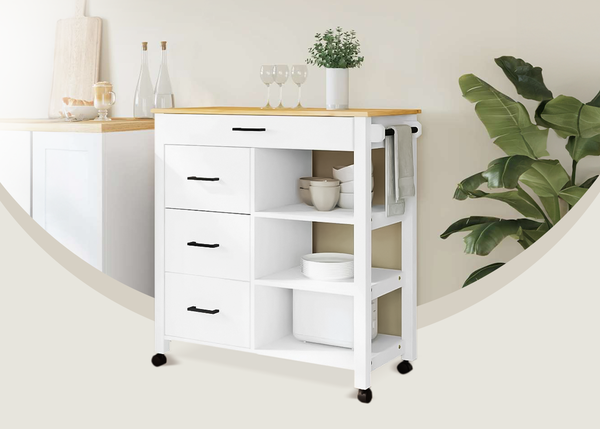 White storage trolley with shelves, drawers and a wooden top placed in a styled kitchen corner next to a large green plant.
