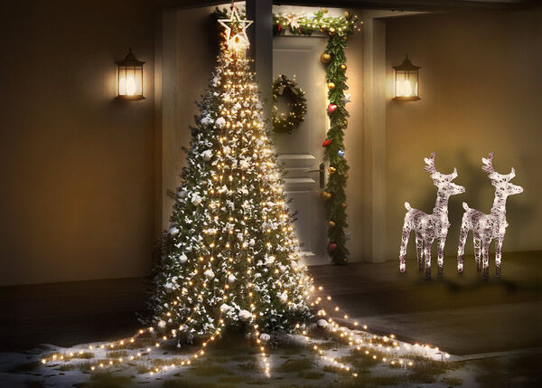 Warmly lit front porch decorated for Christmas, featuring a large, brightly lit Christmas tree, two reindeer decorations, and an illuminated doorway garland and wreath.