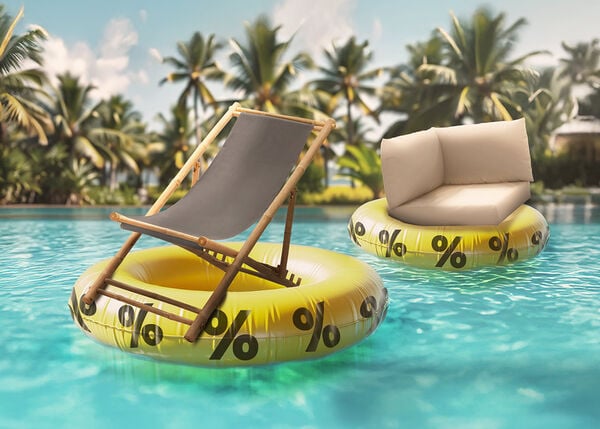 A bamboo deck chair and a pallet cushion each floating on yellow inflatable rings with black percent signs, in a sunny pool surrounded by palm trees.