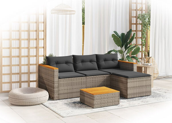 Modular rattan outdoor sofa with dark gray cushions, matching coffee table on rug in a styled terrace. Set against white curtains and trellis with plants.