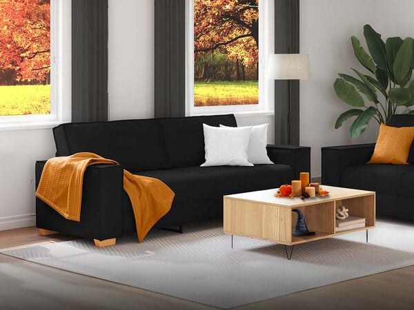 Black sofa with orange blanket and two white pillows, next to a wooden coffee table with Halloween decorations, in a styled living room with an autumn forest view from the windows. Click to see the products in the collection.