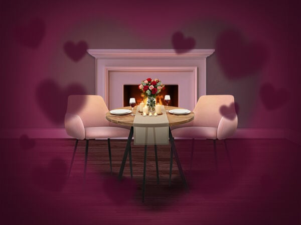 Romantic dining setup with a small round table set for two, pink upholstered chairs, candles and a bouquet of roses, placed in front of a lit fireplace, with soft heart-shaped overlays creating a Valentine&rsquo;s Day atmosphere. Click to see the items in promotion.