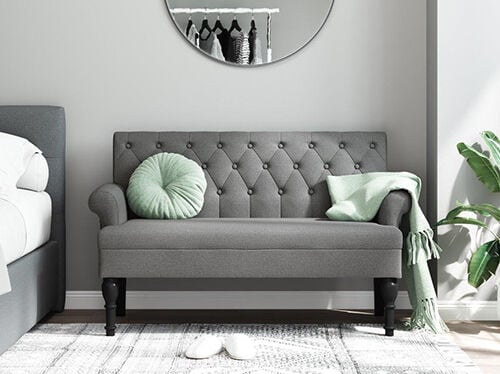 Grey tufted sofa indoors with a light green cushion and a light green blanket on the armrest, decorative mirror on the wall behind. Click to see new arrivals.