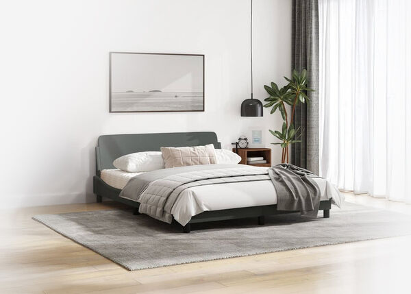 A cozy bedroom with a neatly made bed, a framed picture above the headboard, a brown wooden nightstand, a green potted plant, and a black metal pendant light hanging from the ceiling.