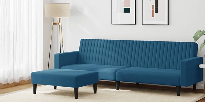 A navy-blue two-seater sofa with a matching footstool, a green plant beside it, a floor lamp behind, and a decorative painting on the wall. Click to discover more new arrivals.