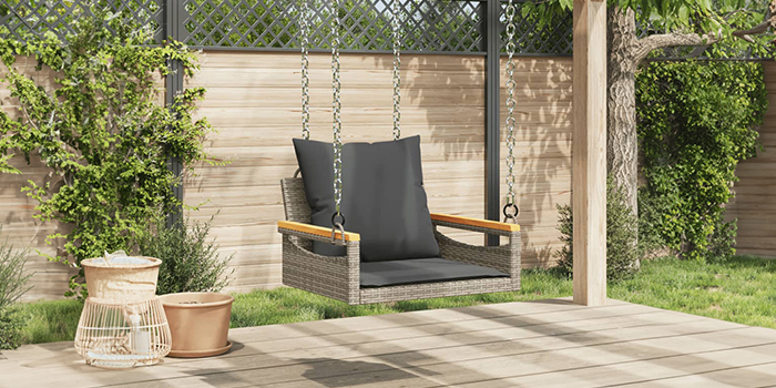 Rattan outdoor swing chair with dark cushions, suspended from wooden beam on patio. Click to see the products in the collection. 