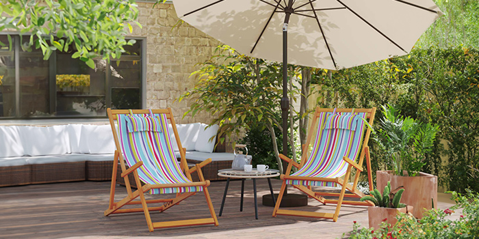 Two wooden deck chairs with colorful striped fabric, small round table, and beige umbrella on garden patio. Click to see the products in the collection. 